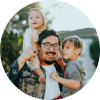 Uomo sorridente che porta due bambini piccoli sulle spalle all'aperto.
