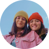Due giovani donne con cappelli colorati che sorridono all'aperto.