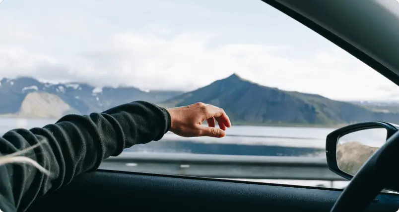 Una mano che si estende dalla finestra di un'auto mentre si guida attraverso i paesaggi mozzafiato dell'Islanda, rappresentando l'affidabile assistenza stradale di Cars Iceland per un viaggio senza preoccupazioni.