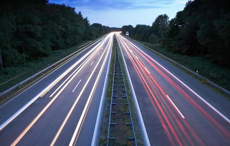 Autostrada di notte con scie luminose bianche e rosse create dai fari delle auto in movimento.