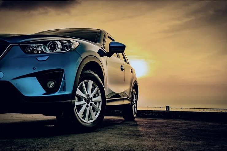 Primo piano di un SUV blu su una strada al tramonto, con il sole basso all'orizzonte e un cielo dorato sullo sfondo.