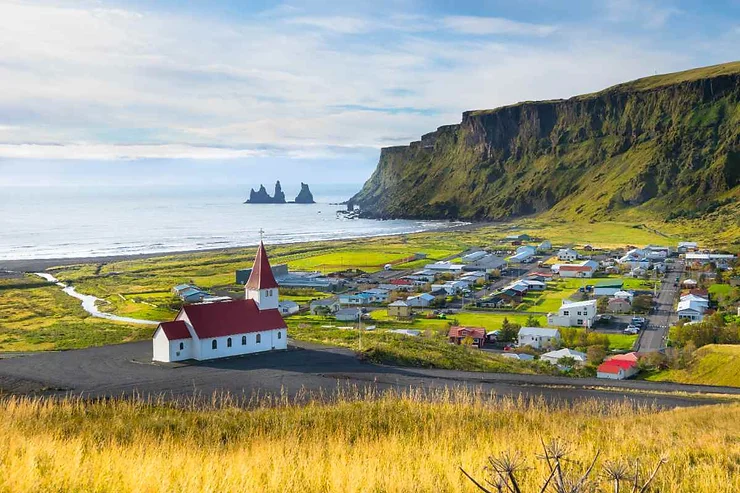 Vista panoramica di Vik in Islanda, con una chiesa rossa e bianca, scogliere verdi e l'oceano in lontananza.