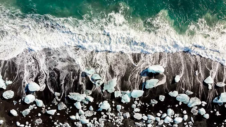 Vista aerea della spiaggia dei diamanti in Islanda, con onde bianche e blocchi di ghiaccio sulla sabbia nera.