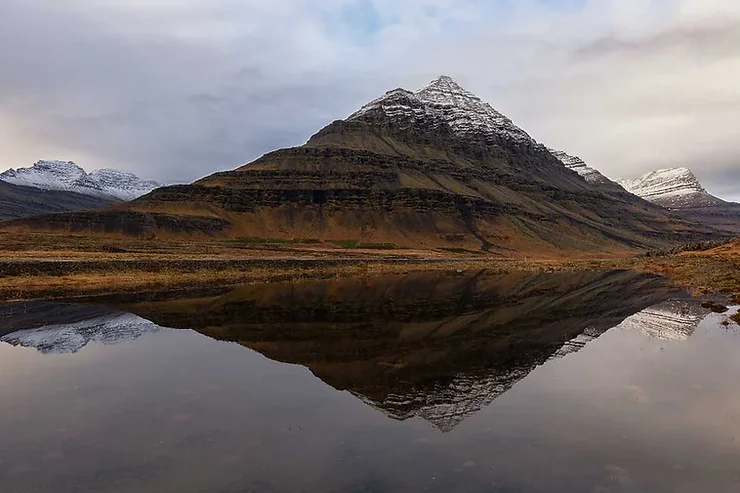 Una montagna innevata si riflette perfettamente nelle acque calme di un lago, creando un panorama suggestivo e speculare in Islanda.