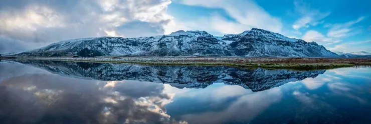 Un panorama mozzafiato con montagne innevate riflesse in un lago cristallino, sotto un cielo parzialmente nuvoloso.