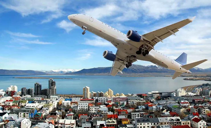 Aereo che sorvola una città costiera islandese con vista su mare e montagne.
