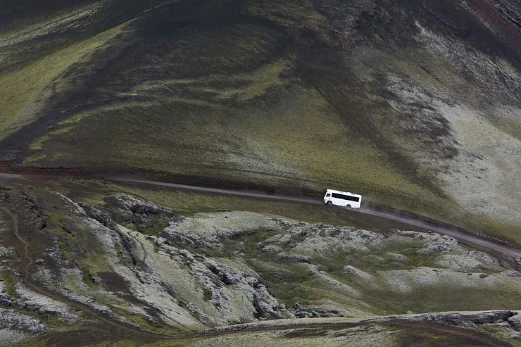 Autobus bianco su una strada isolata tra montagne e paesaggi brulli islandesi.