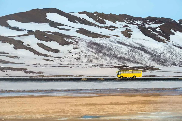 Autobus giallo che attraversa pianure e colline innevate in Islanda.