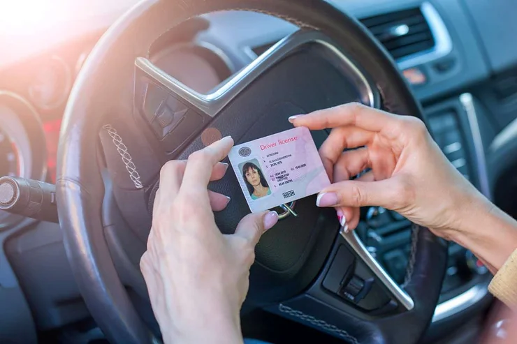 Una persona sostiene una patente di guida all'interno di un'auto, preparandosi a guidare.