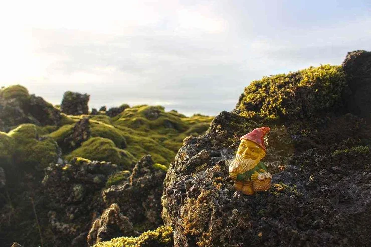 Statua di un elfo sorridente su rocce coperte di muschio.