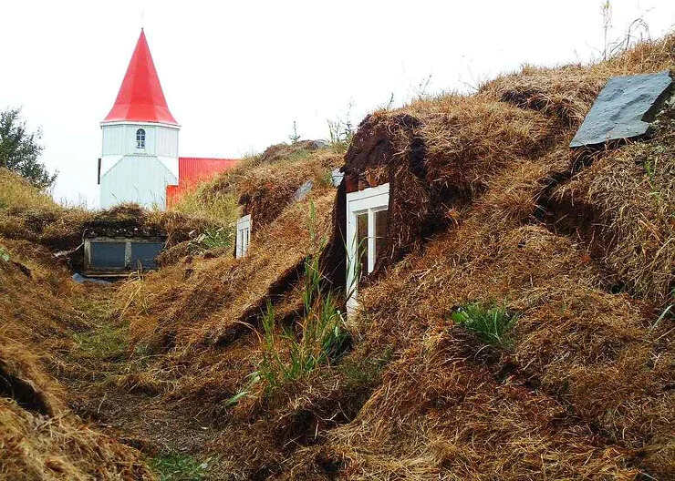 Case sotterranee in Islanda con chiesa rossa sullo sfondo.
