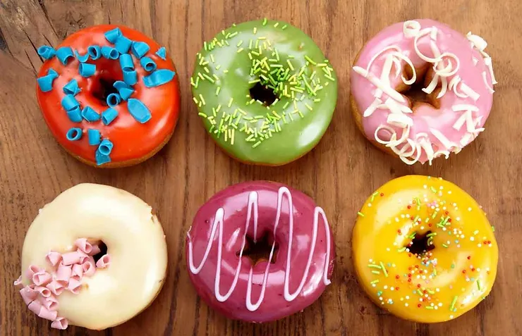 Sei ciambelle glassate in vari colori vivaci con decorazioni come scaglie e zuccherini.