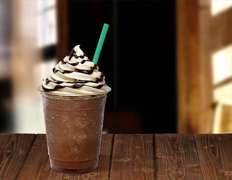 Una bevanda frappuccino con panna montata e decorazioni al cioccolato su un tavolo di legno.