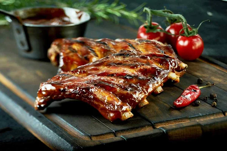 Costine di maiale glassate con salsa barbecue, servite con pomodorini e peperoncino.