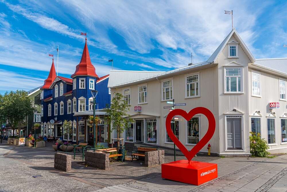 Centro di Akureyri in Islanda con edifici colorati e un’installazione a forma di cuore rosso, sotto un cielo azzurro e nuvole bianche.