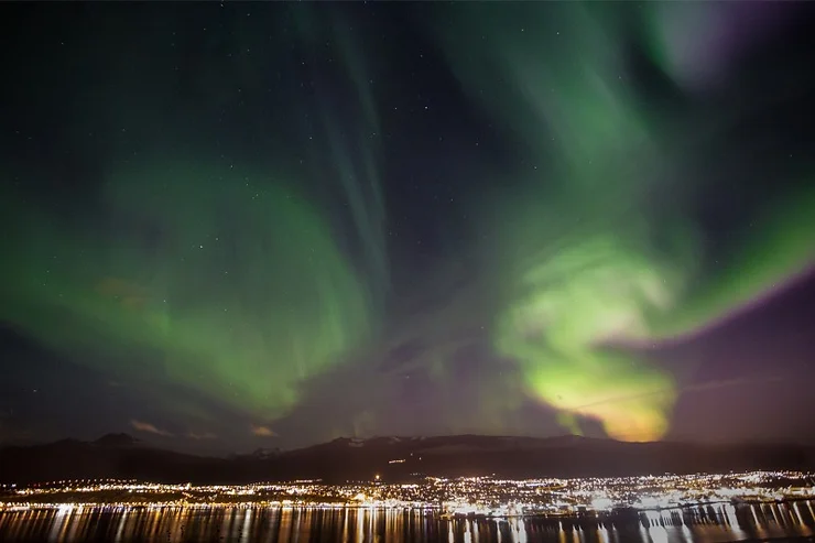 L'aurora boreale verde danza nel cielo notturno sopra la città di Akureyri, riflettendosi sulle acque sottostanti.