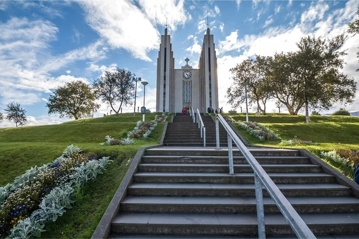 La Chiesa di Akureyri, con una scalinata in pietra circondata da un giardino ben curato sotto un cielo limpido.