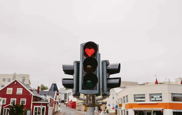 Un semaforo unico con una luce rossa a forma di cuore, posizionato in una strada di una città con edifici colorati sullo sfondo.
