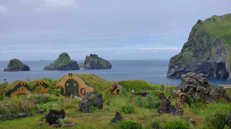 Come si Chiamano le Case degli Elfi? Casette degli elfi sull'isola di Heimaey in Islanda, circondate da paesaggi verdi e rocce vulcaniche con vista sull'oceano.