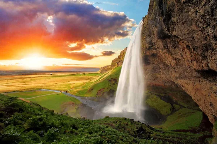 Un tramonto spettacolare con la cascata Seljalandsfoss in primo piano e campi verdi.