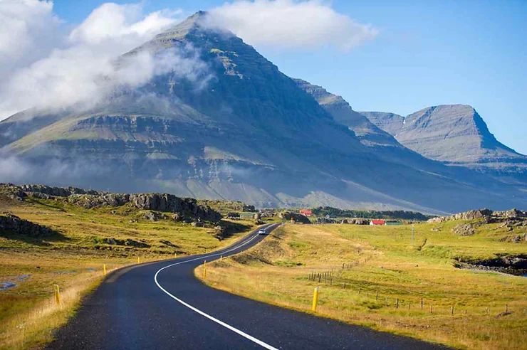 Una strada asfaltata che serpeggia attraverso una valle verde con montagne maestose sullo sfondo.
