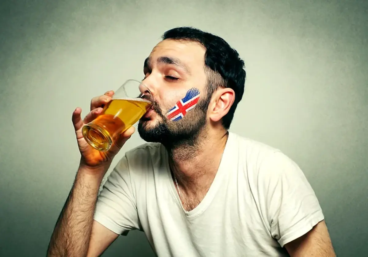Uomo che beve una birra con una bandiera islandese dipinta sulla guancia. Perfetta per rappresentare la cultura birraria dell'Islanda.