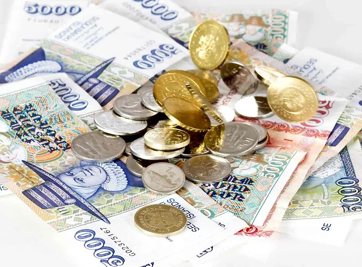 Una pila di banconote islandesi da 5.000 corone, accompagnata da monete d'oro e d'argento sparse. Il denaro è disposto in modo casuale su una superficie bianca, mettendo in evidenza la ricchezza e il design delle banconote.