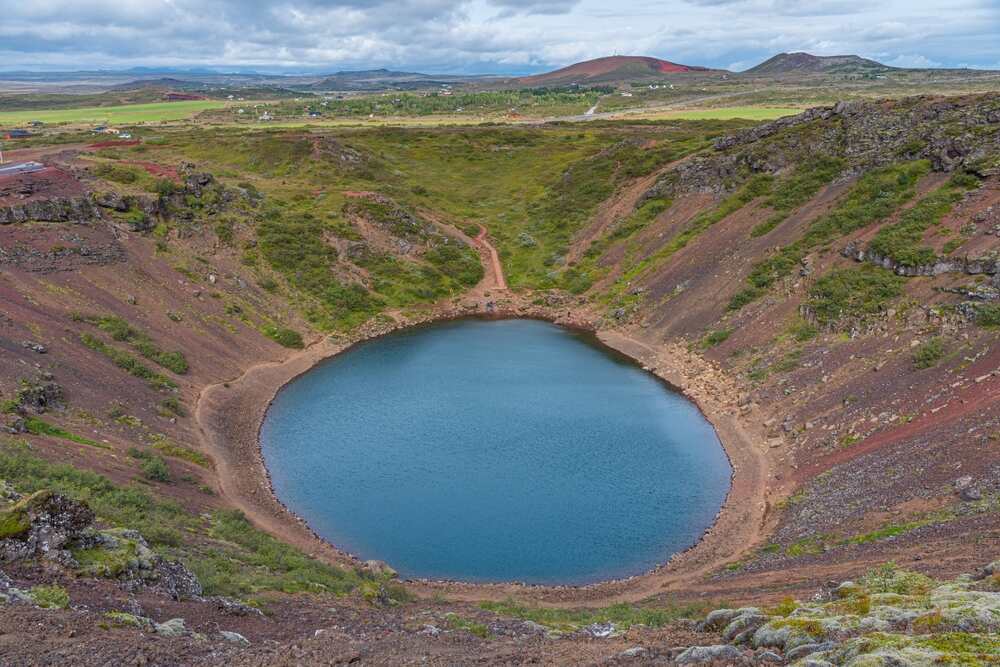 Vista panoramica del cratere di Kerið, un lago vulcanico circondato da pareti di roccia e vegetazione, immerso in un paesaggio verde islandese.