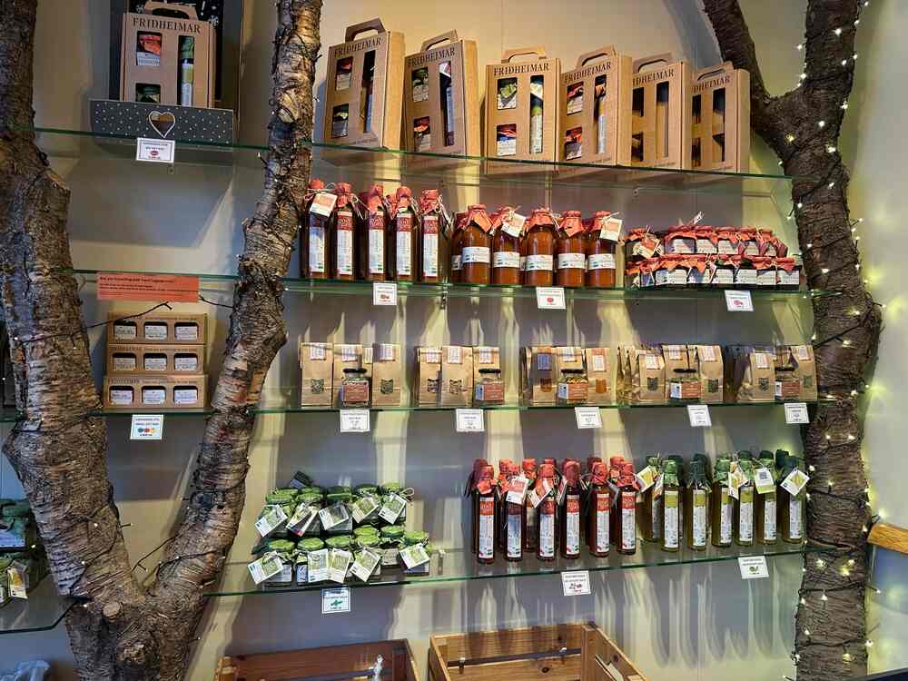 Il posto migliore per acquistare maglioni in Islanda Un'immagine che mostra uno scaffale in un negozio in Islanda. Lo scaffale è decorato con rami di alberi e ospita prodotti locali come marmellate, succhi, olio e confezioni regalo. Le confezioni hanno etichette dai colori vivaci.