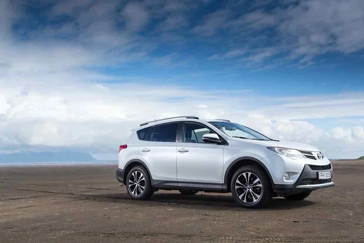 Un SUV bianco parcheggiato in un paesaggio aperto e pianeggiante, con un cielo azzurro e nuvole in lontananza.