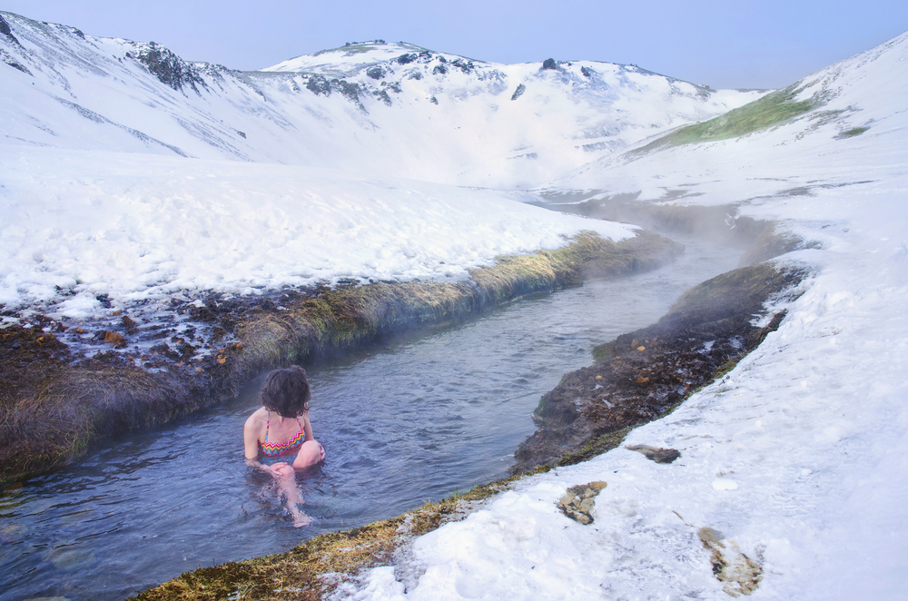 Donna che si rilassa nel fiume caldo di Reykadalur, Islanda, circondata da neve e vapore termale in un paesaggio invernale mozzafiato.