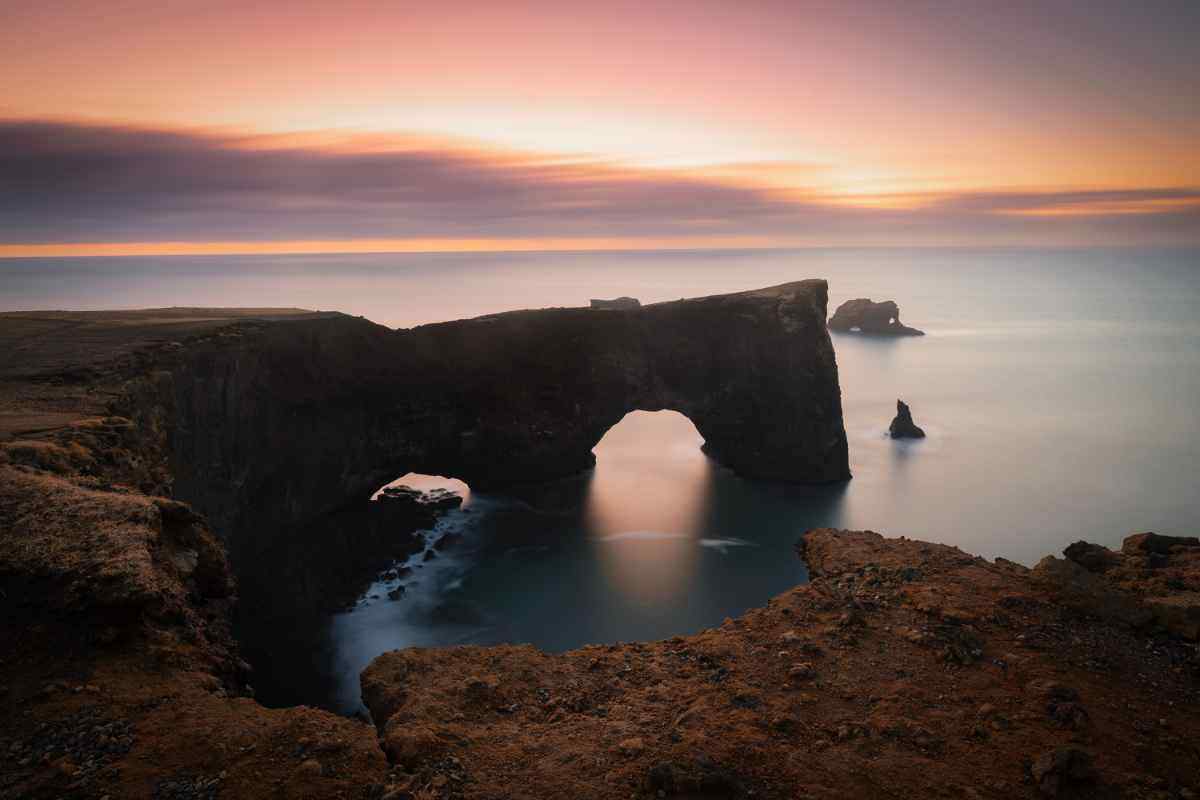 Vista panoramica dell’arco roccioso di Dyrhólaey in Islanda al tramonto, con scogliere vulcaniche che si affacciano sull’oceano Atlantico.