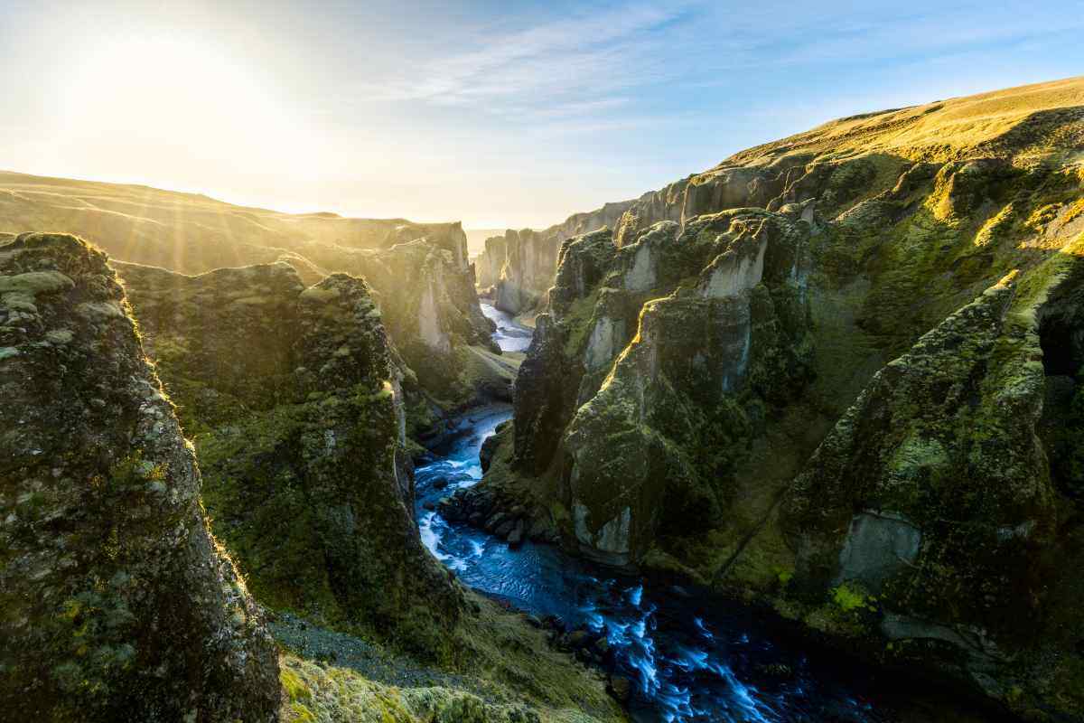 Vista panoramica del canyon Fjaðrárgljúfur in Islanda al tramonto, con alte pareti ricoperte di muschio e fiume glaciale che scorre alla base.