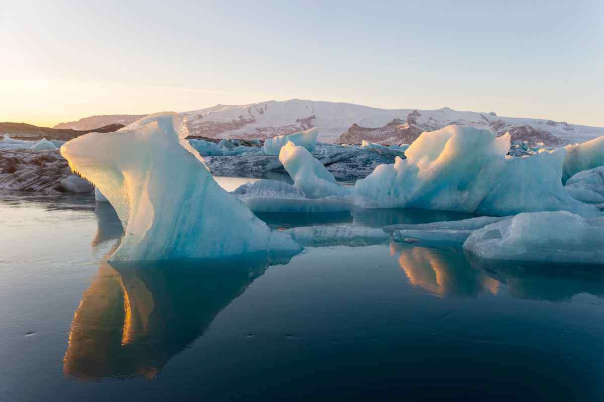 Iceberg galleggianti nella laguna glaciale di Jökulsárlón in Islanda, illuminati dalla luce del tramonto con montagne innevate sullo sfondo.