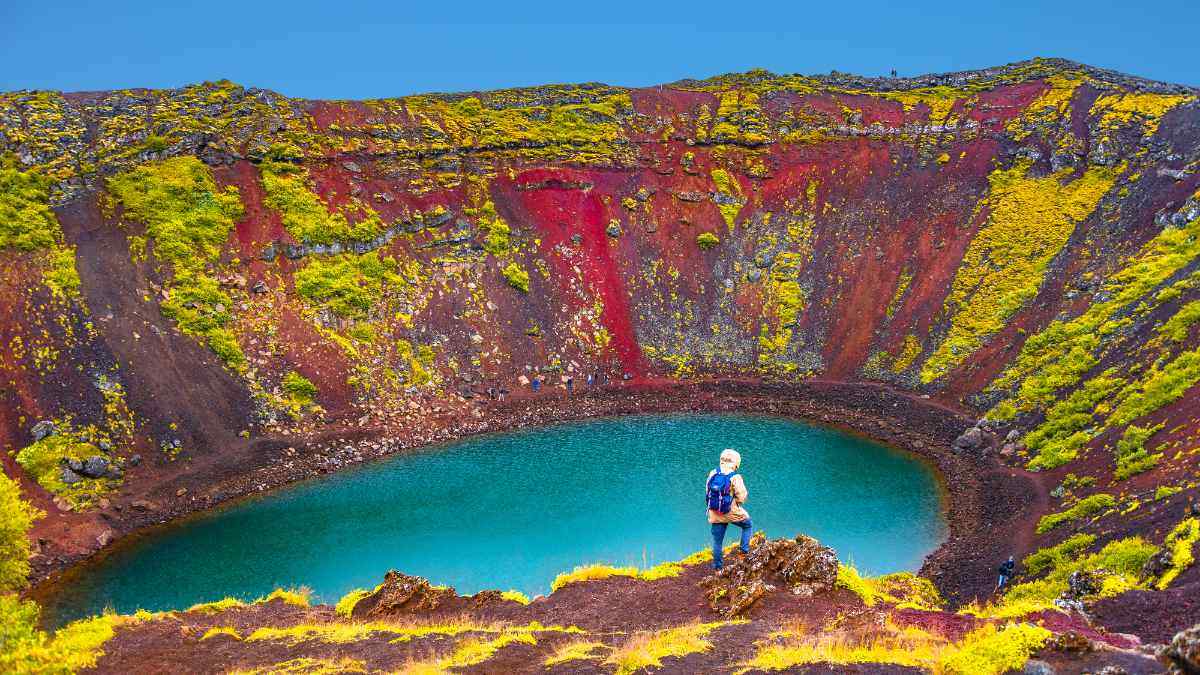 Escursionista davanti al cratere vulcanico Kerið in Islanda, con pareti rosse, muschio verde e lago color turchese nel cuore del Golden Circle.