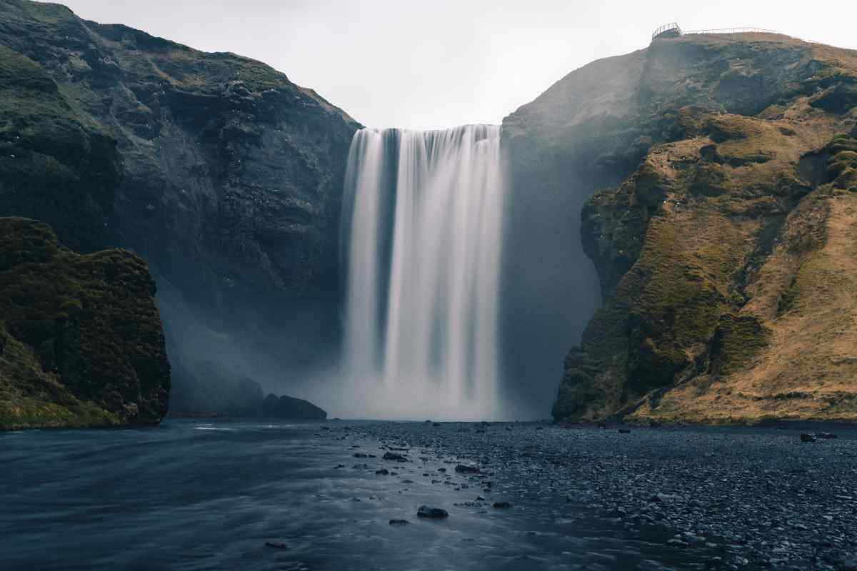 La cascata Skógafoss in Islanda, con il suo salto verticale imponente tra le scogliere verdi e il fiume che scorre alla base.