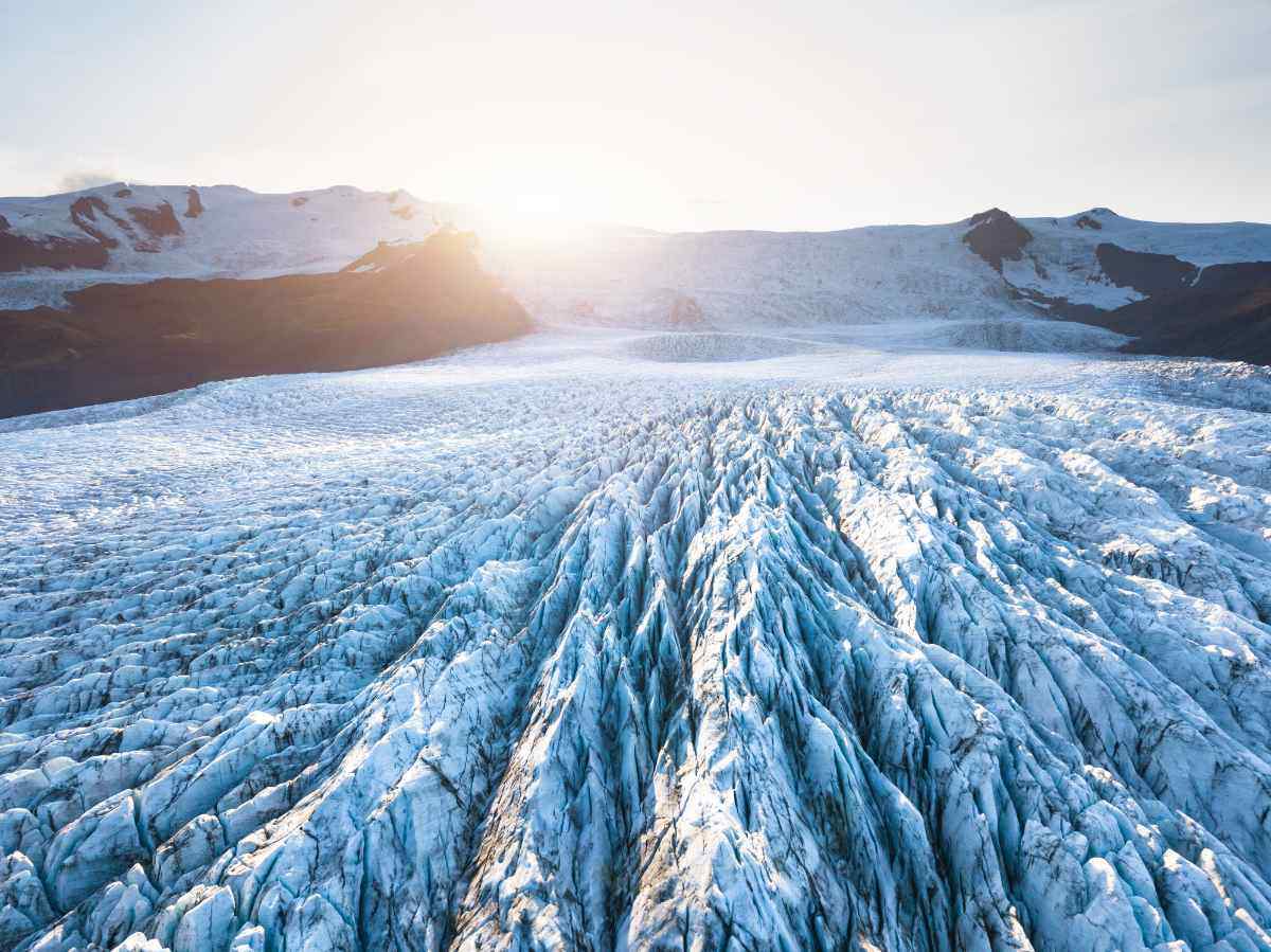 Vista aerea del ghiacciaio Vatnajökull in Islanda al tramonto, con crepacci e striature di ghiaccio che si estendono fino all’orizzonte.