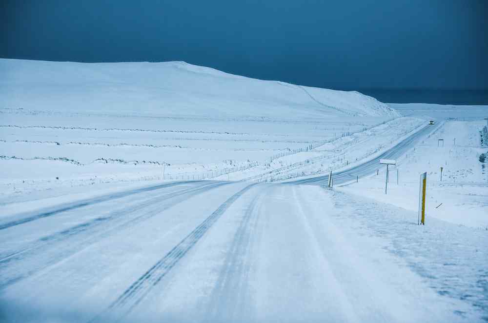 Strada rurale ghiacciata che attraversa un paesaggio islandese innevato sotto un cielo scuro.