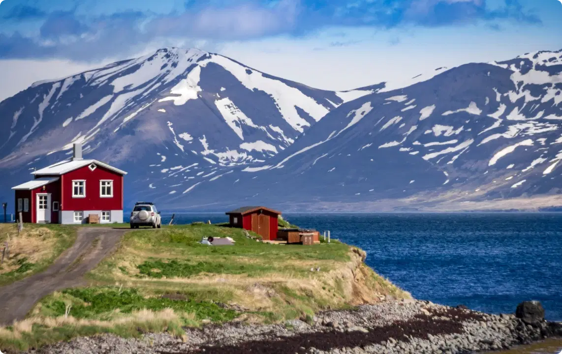Una pittoresca casa islandese vicino all’acqua, con montagne innevate sullo sfondo, è il punto di partenza perfetto per un viaggio on the road in Islanda. Puoi ritirare un’auto a noleggio dall’Aeroporto Internazionale di Keflavik per la tua avventura, scegliendo tra auto per passeggeri, veicoli elettrici e modelli di lusso per un’esperienza indimenticabile.